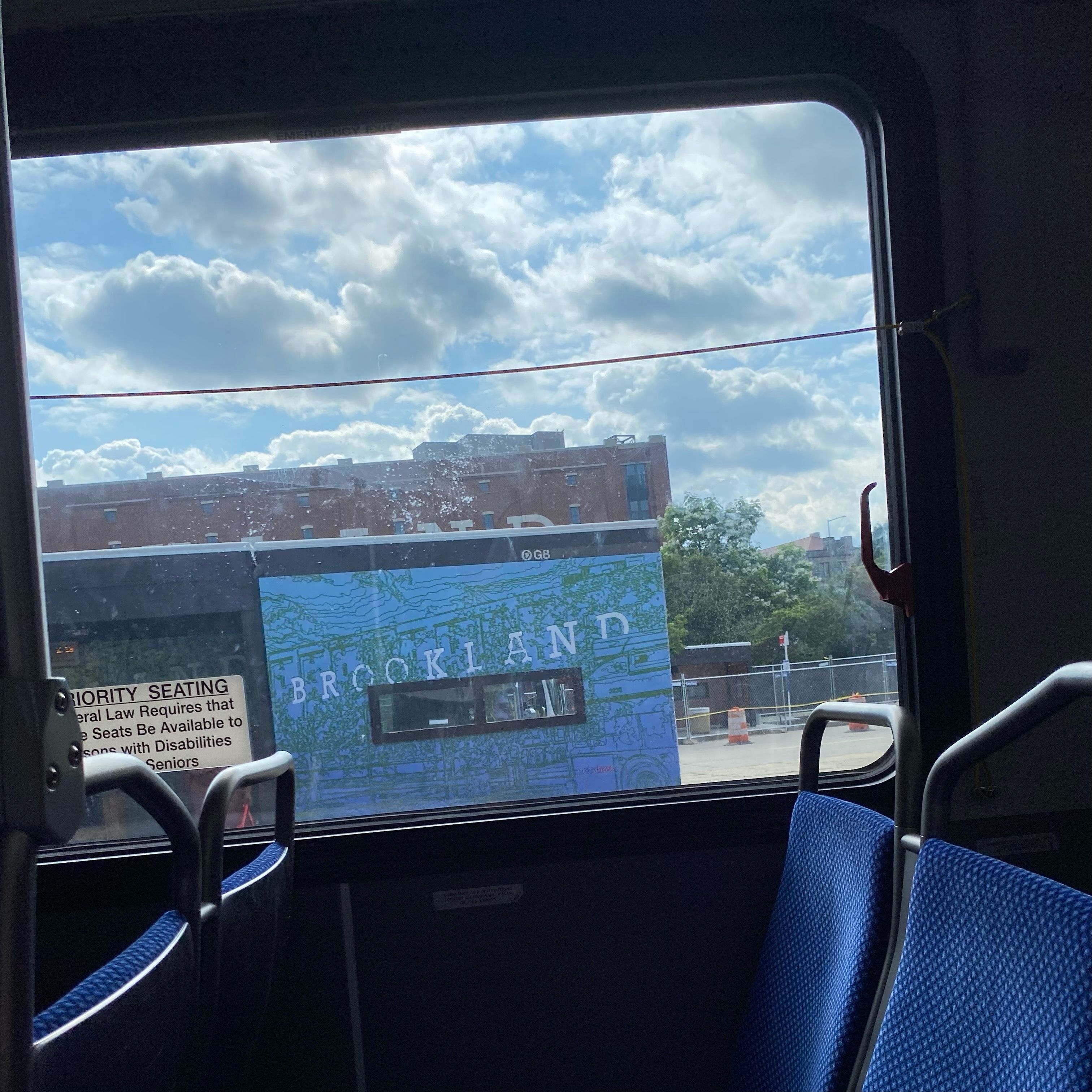 A bus window with a view of a cloudy blue sky and a blue wall that says Brookland.