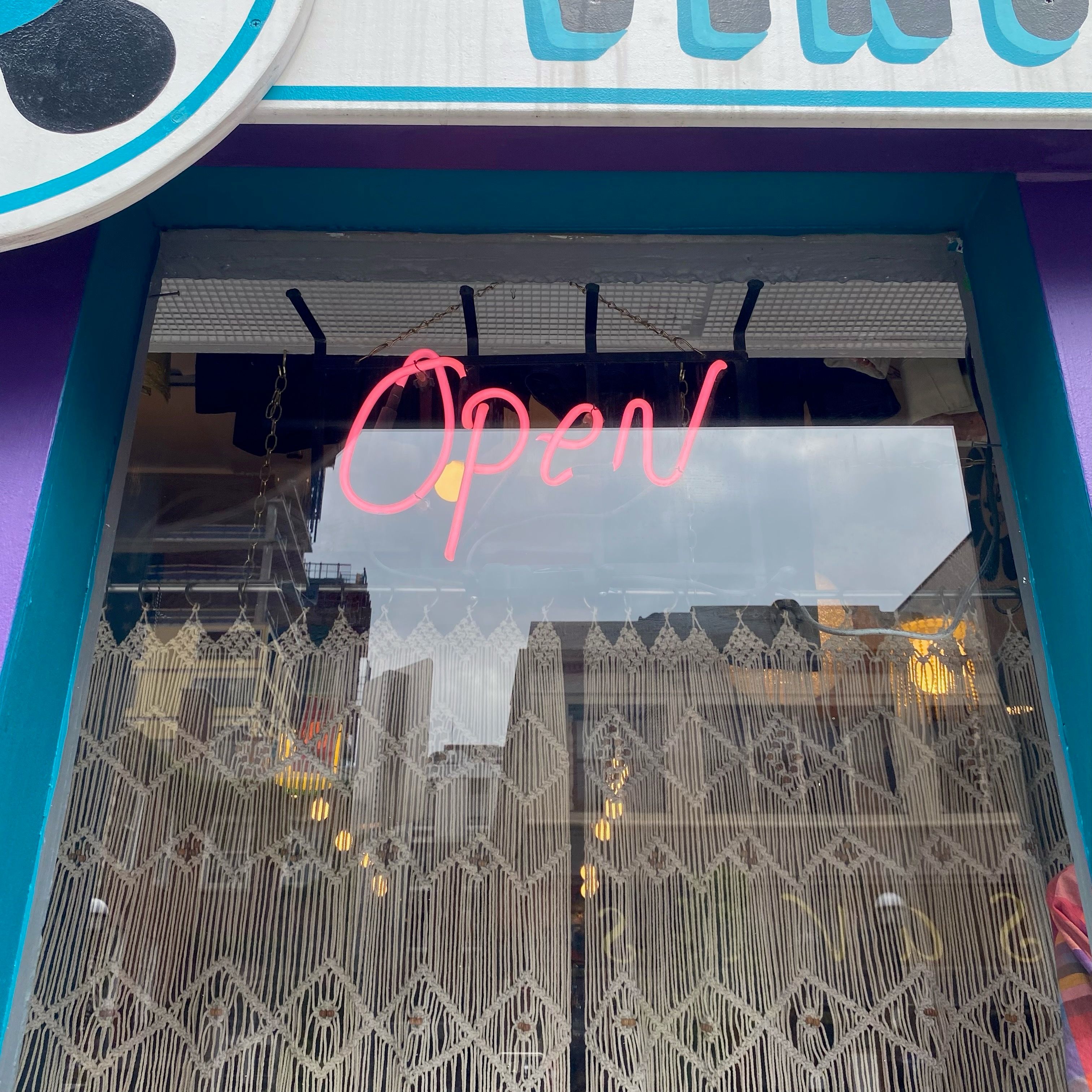 A window with a blue border that has a view of a neon red open sign.