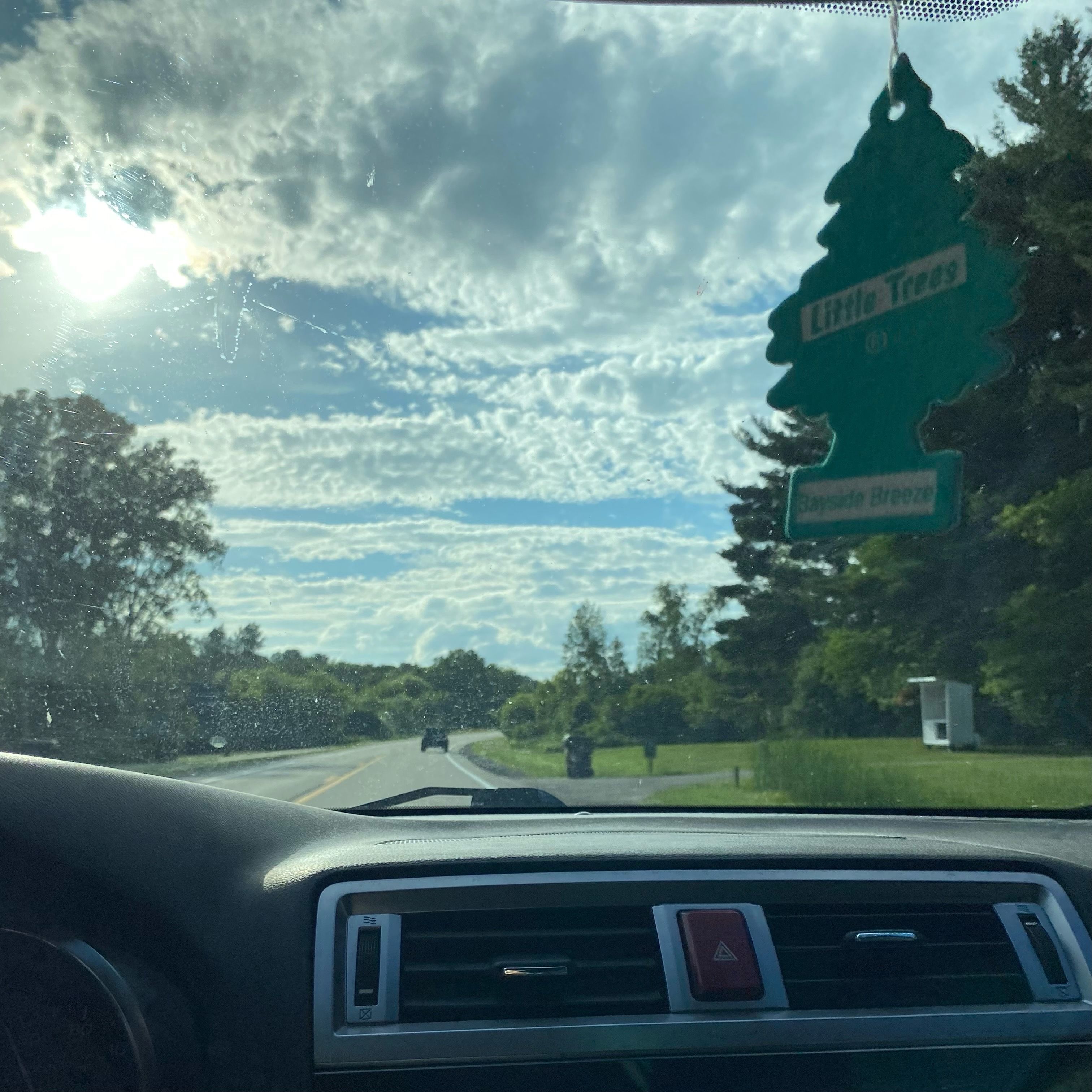 Car window with a view of the sun peaking through the clouds.