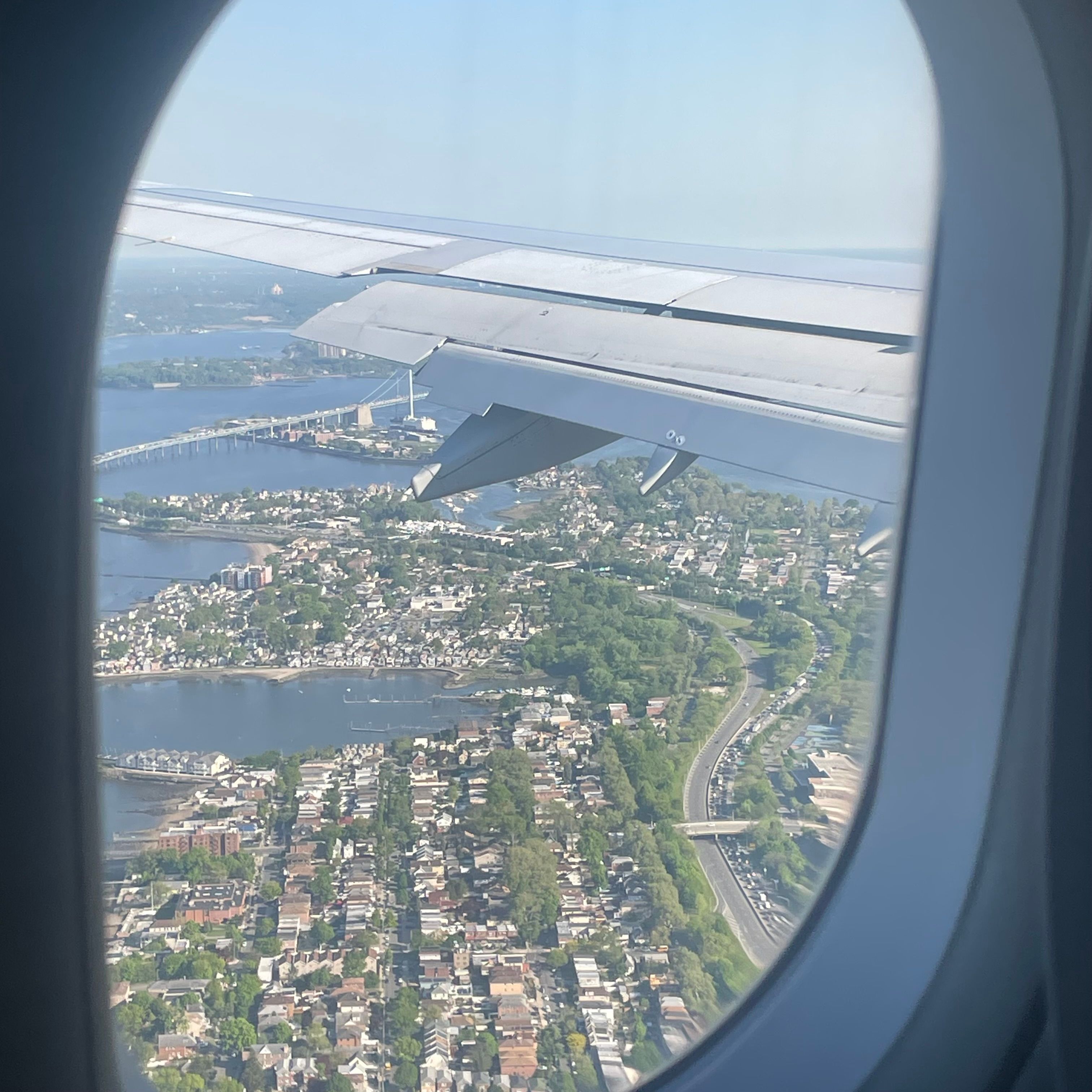 An airplane window with a view of the sea and several single story buildings. The wing of the airplane is visible.