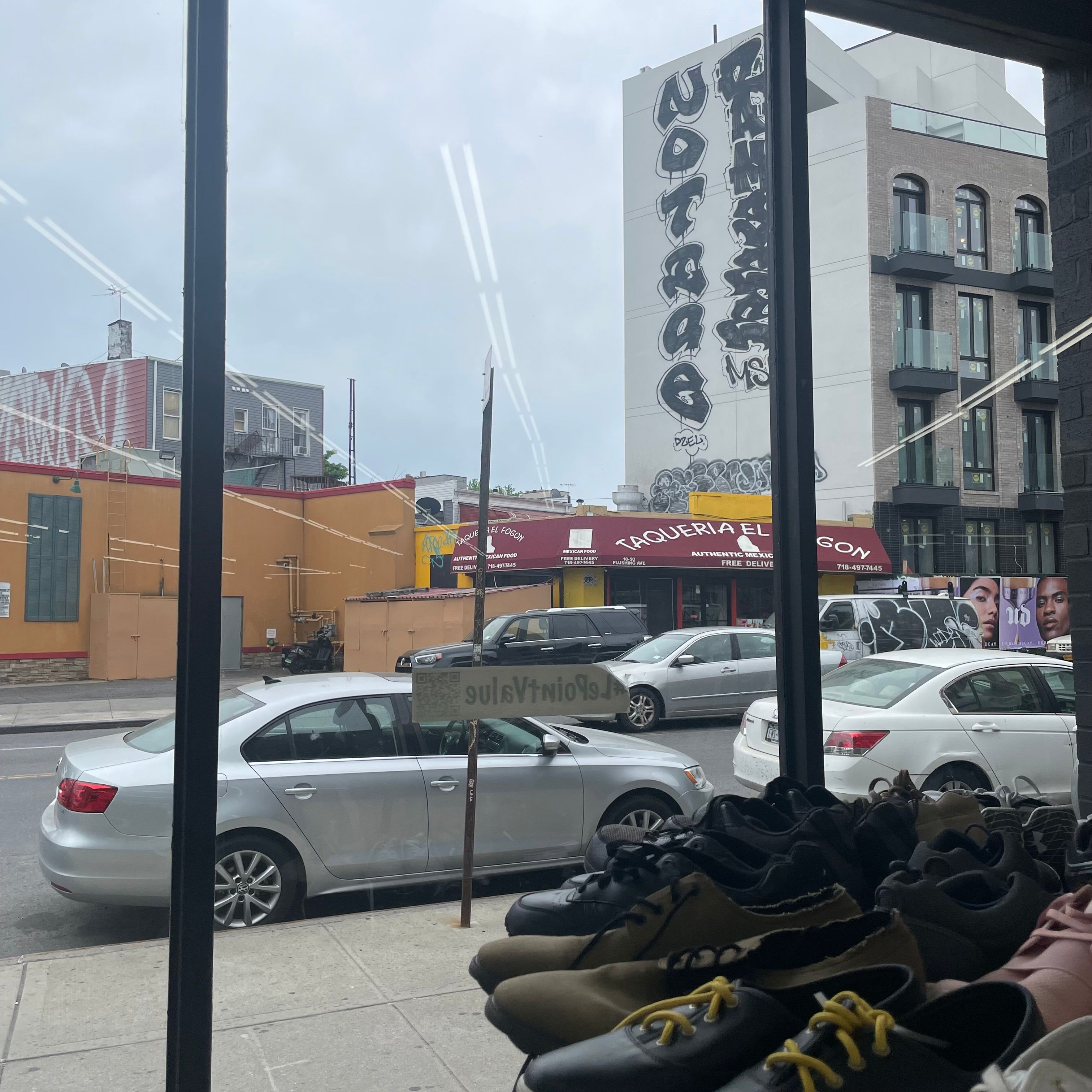 A rack of shoes with a window in the background. The window has a view of several cars and buildings with graffiti.