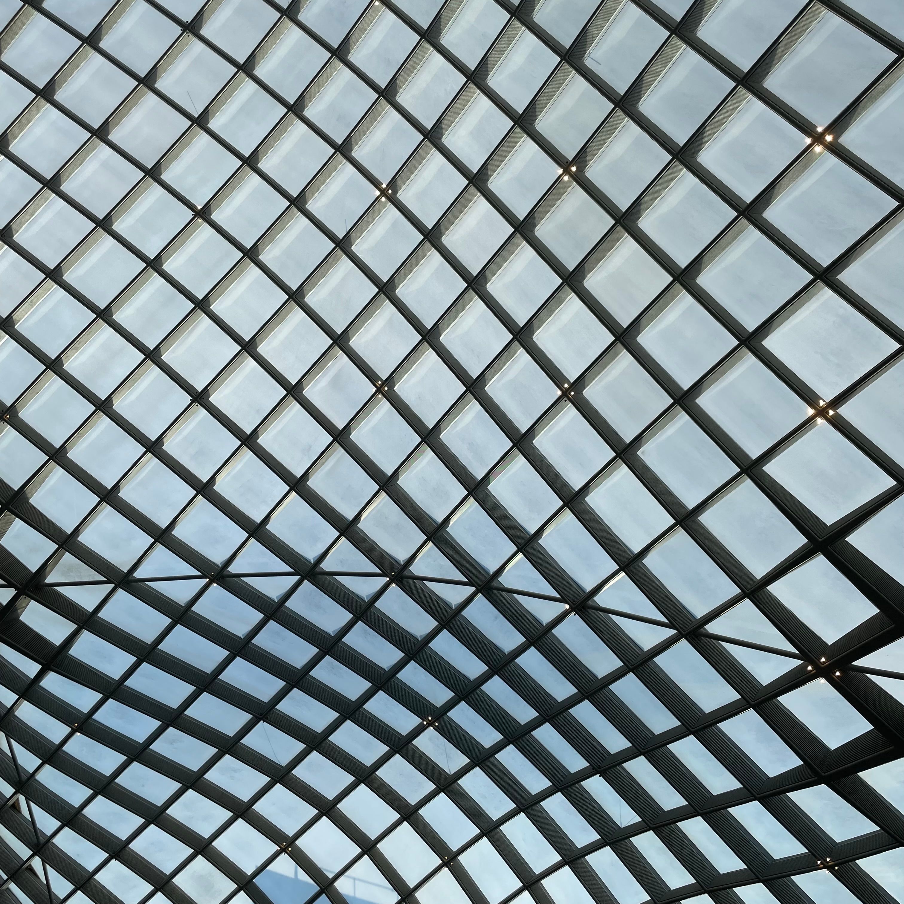 A curved lattice frame of glass cells with a view of the blue sky.