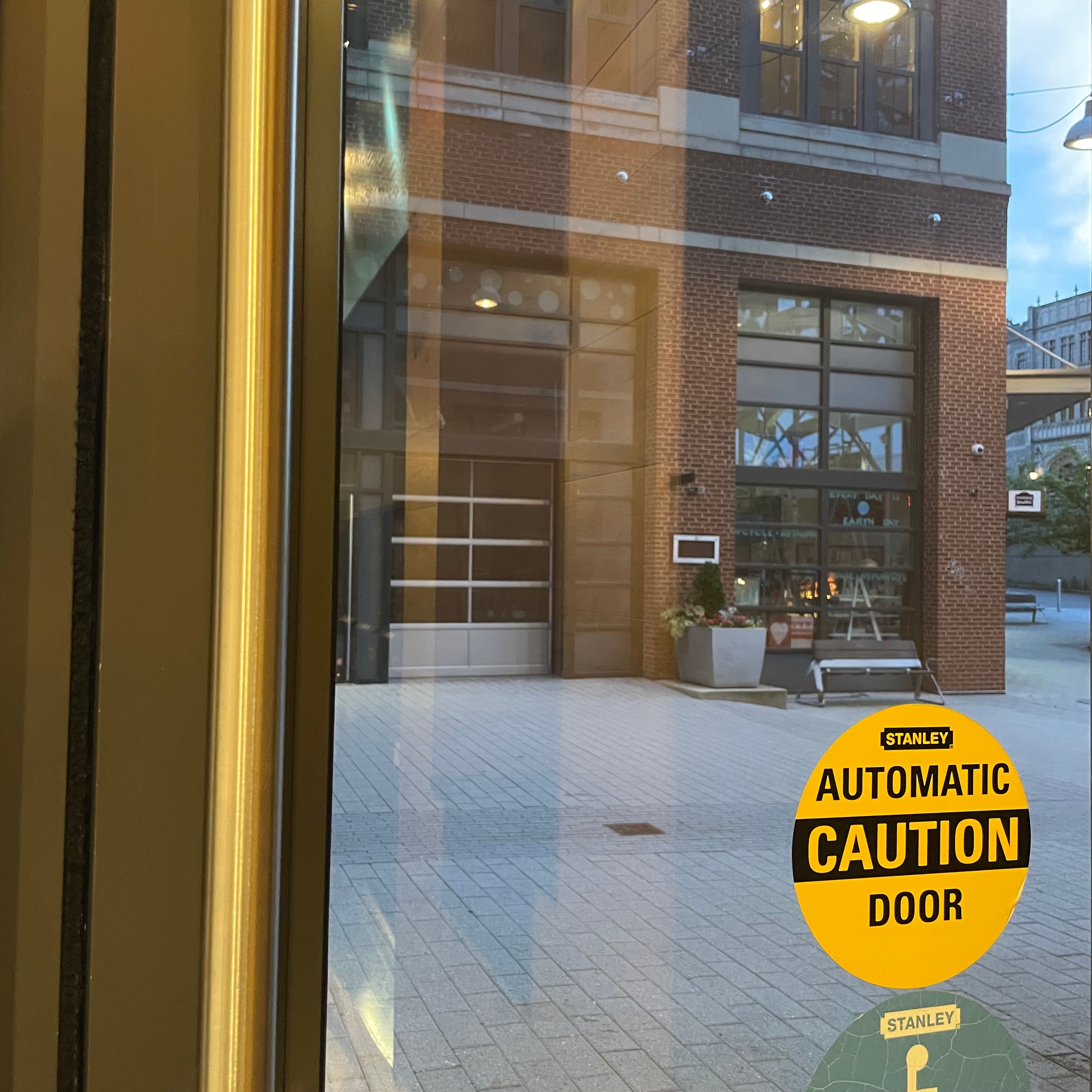 A door window with a automatic caution sticker. The window has a view of a brick building across the street.