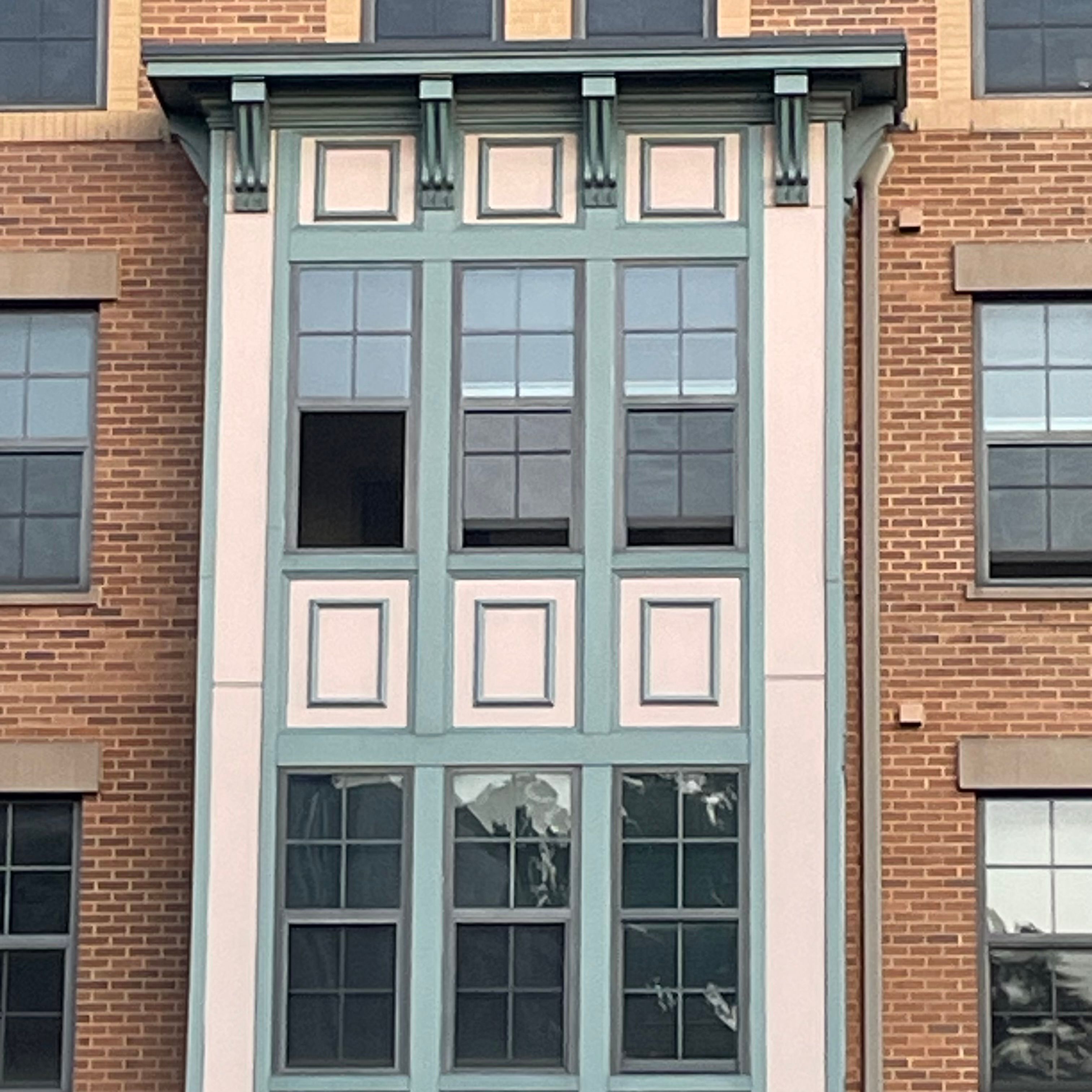 A brick wall with a grid of windows. There is a protuding center area of windows outlined by beige and turquoise wall.