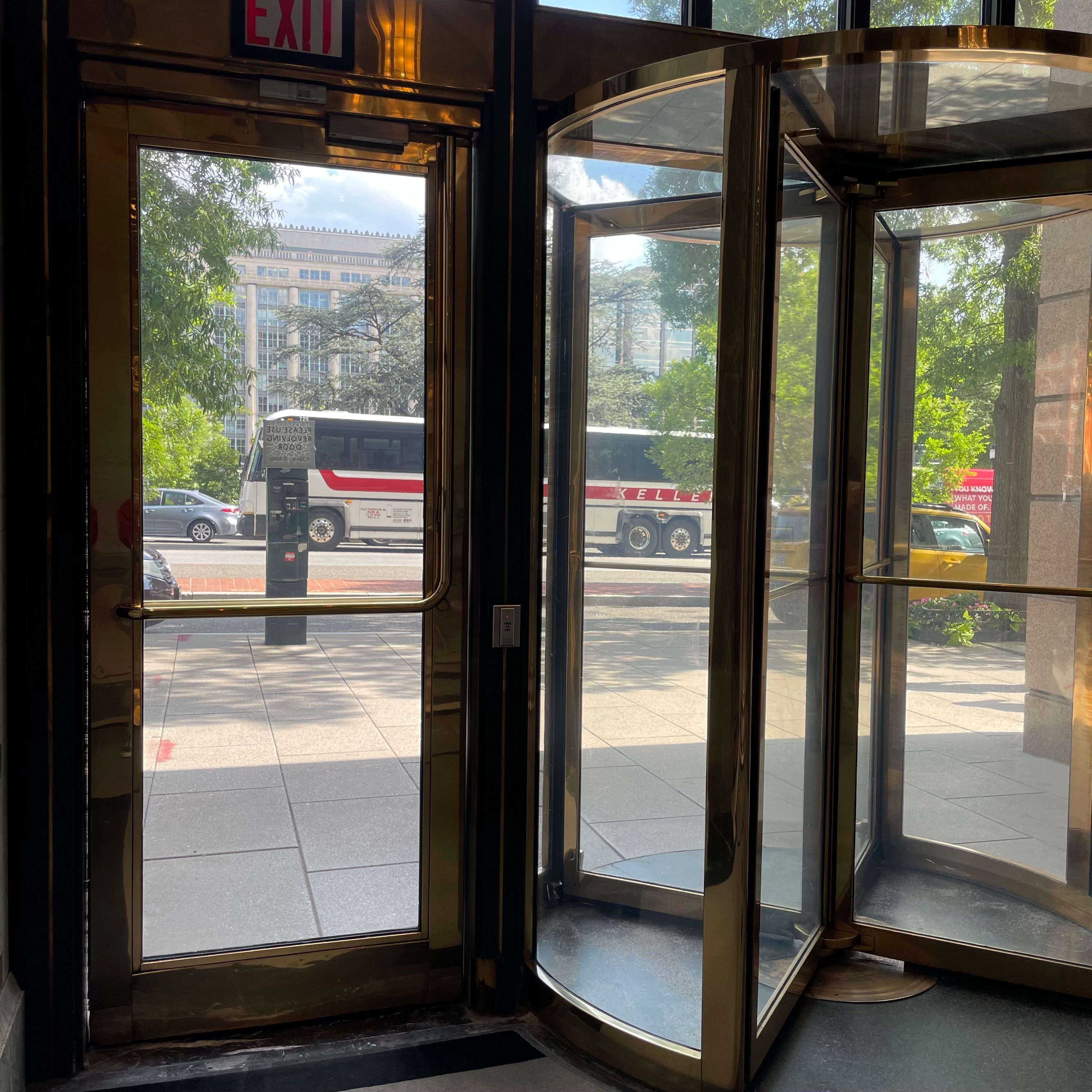 A door window next to a revolving door. There is a view of a bus.